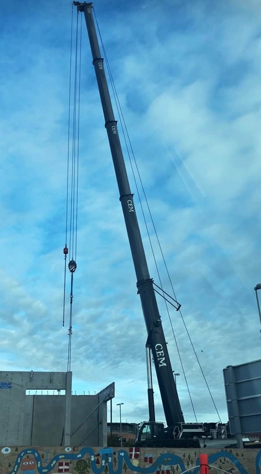 Mobilkran med bommen fuldt udskudt over et betonbyggeri